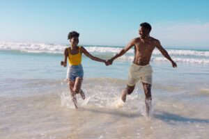 couple holding hands and running through shallow water on beach